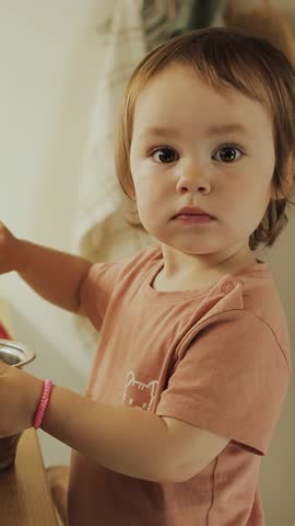 Vertical video. Smiling 3 year old girl cooking in the kitchen, holding a pan. Wonderful and cute cooking moment, child helping mom