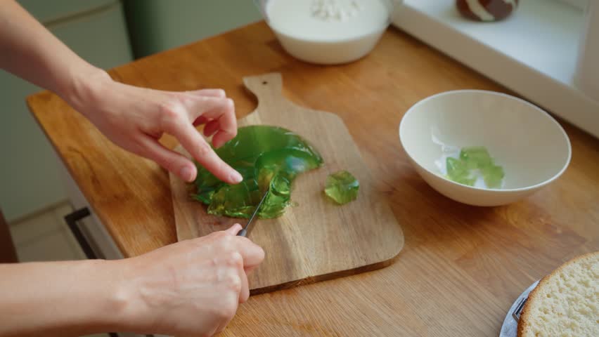 Woman cutting homemade jelly with knife on wooden cutting board for cake filling preparation. Female slicing homemade jelly into pieces for dessert. Lady preparing jelly for cake filling on wooden