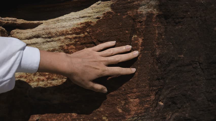 Female hand gently touching rough sandstone texture, connecting with nature through organic patterns and raw natural surfaces. Earthy tones and tactile sensations.