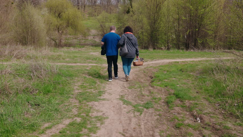 Middle-aged couple walking through a forest path as the woman supports the limping man on their way to a picnic. High quality 4k footage