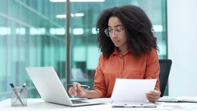 Busy african american businesswoman is doing paperwork using a laptop computer sitting at a workplace in business office. Focused female financier deals with financial reports, engaged in accounting - Powered by Shutterstock - Get 15% off with code: PIKWIZARD15