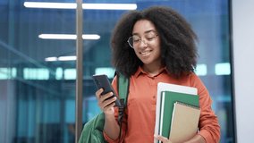 Smiling african american female student is using mobile phone standing at university indoors. Happy black woman with backpack browsing social media, chatting online or typing reading message. Close up - Powered by Shutterstock - Get 15% off with code: PIKWIZARD15