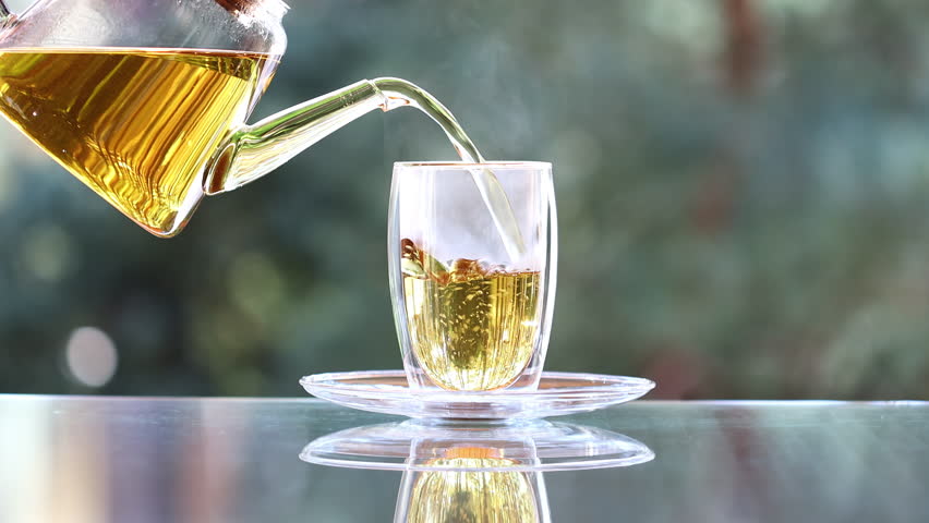 Pouring Herbal Tea into a Glass Cup with a Beautiful Rose Bouquet. Tea in the Glass Teacup. Relaxing Tea Time with Pink Roses and a Glass Teacup