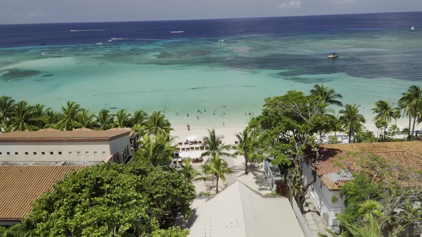Drone flies low over houses and trees toward white sandy beach in West Bay, Roatán, Honduras