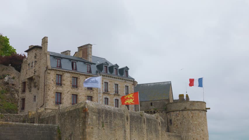 The high walls of the Mont-Saint-Michel Abbey, the ancient building and the flags of France and the Duchy of Normandy fluttering on them.