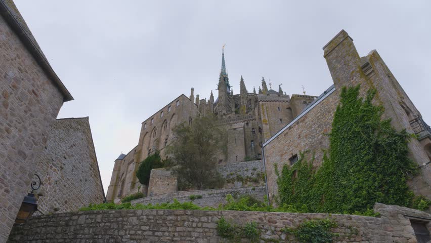 View of the Mont-Saint-Michel Abbey walls against a blue sky and clouds on a windy spring day. The Mont-Saint-Michel Abbey is an abbey located within the city and tidal island of Mont-Saint-Michel.