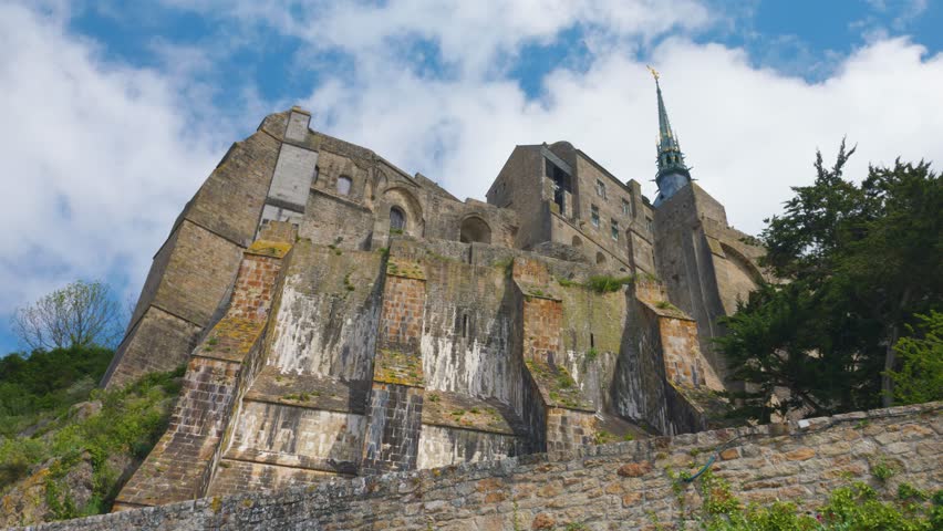 View of the Mont-Saint-Michel Abbey walls against a blue sky and clouds on a windy spring day.