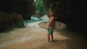 Sporty old man holds a surfboard on seashore. Senior male surfs in Bali, surfing on Uluwatu beach. Travelling elderly people enjoying retired lifestyle on tropical island vacation trip. Portrait - Powered by Shutterstock - Get 15% off with code: PIKWIZARD15