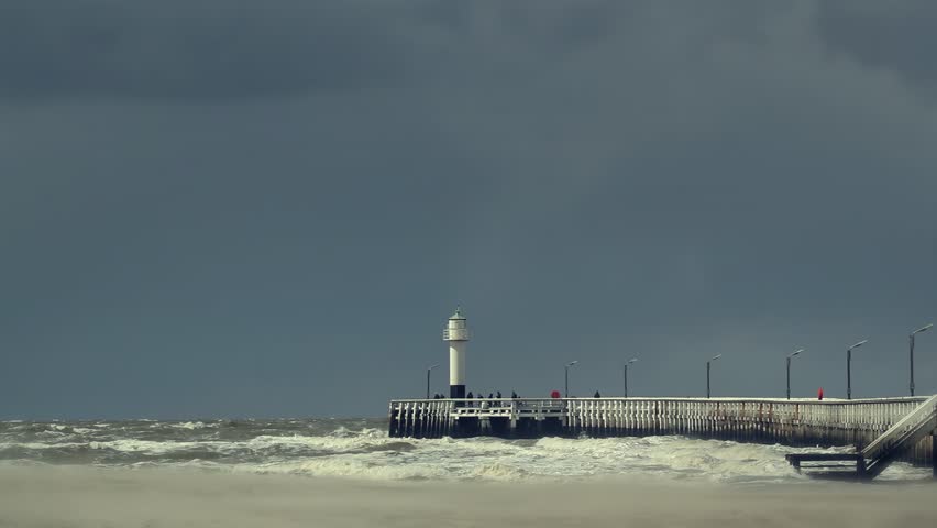 Seascape with vintage wooden pier, waves crashing on the beach and dramatic sky. High tide moody shot on the shoreline of Nieuwpoort-Beach, Belgium. 