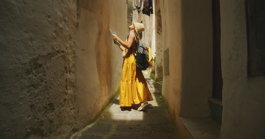 Tourist woman in dress reading a map in a narrow alleyway of Amalfi town Italy