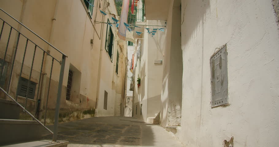 Happy woman walks through a sunlit narrow alley in a coastal Mediterranean town