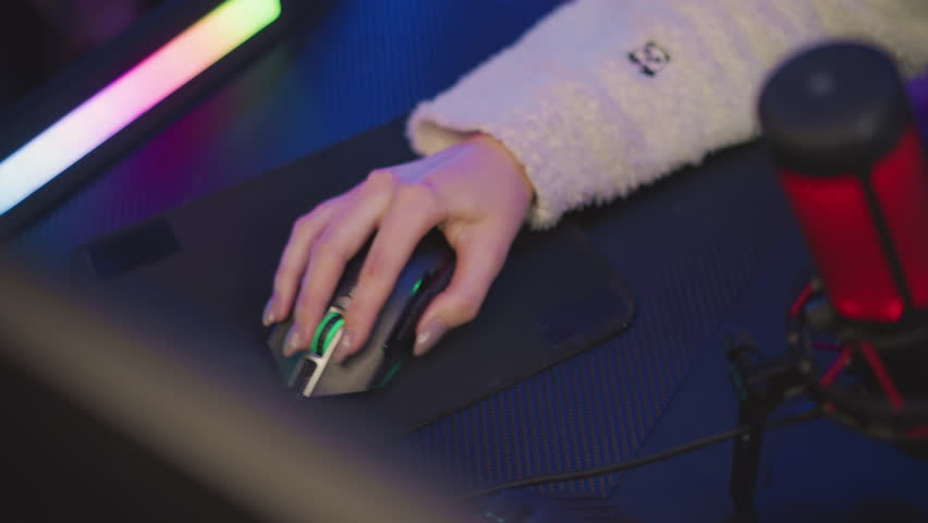 Aerial view of lady hand with polished nail in fluffy sweater featuring teddy bear design using illuminated gaming mouse on black pad, surrounded by colorful ambient lighting and streaming microphone