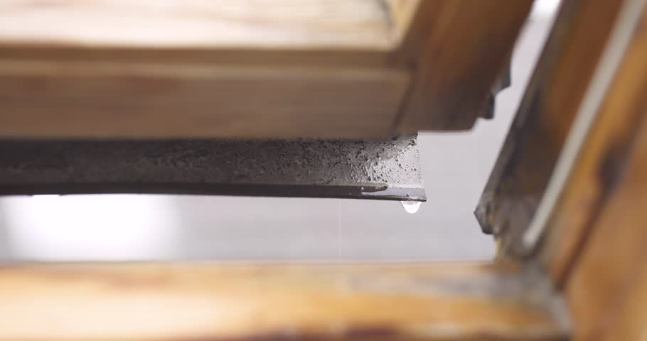 Tight shot of rainwater dripping through an open window, representing leaks and poor insulation.