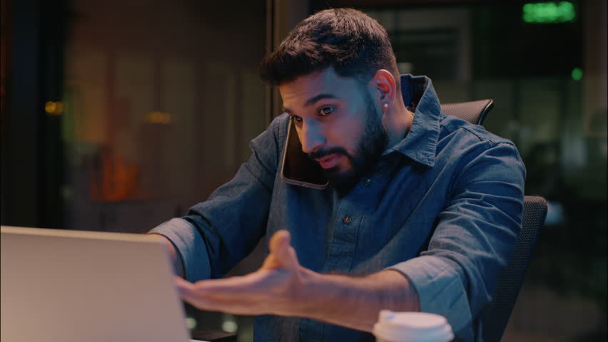 Stressed businessman Indian man guy working in night overtime office Arabian angry frustrated male business entrepreneur dissatisfied talk mobile phone overwork stress problem smartphone call arguing