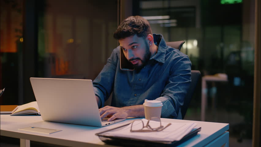 Stressed businessman Indian man guy working in night overtime office Arabian angry frustrated male business entrepreneur dissatisfied talk mobile phone overwork stress problem smartphone call arguing