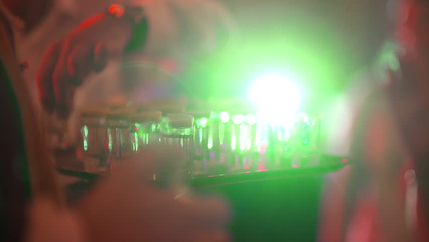 A close-up shot of a man reaching for a vodka glass at a lively party setting.