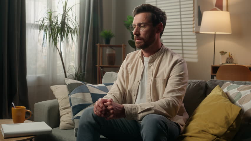 Caucasian man intelligent male guy on couch sofa reading book alone at home adult homeowner reader businessman in glasses read literature paper textbook hobby leisure in apartment studying knowledge