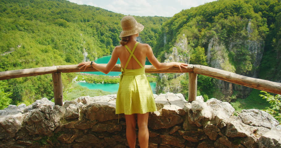 Woman overlooks the vivid blue water and waterfall from rocky viewpoint at Plitvice Lakes National Park in Croatia
