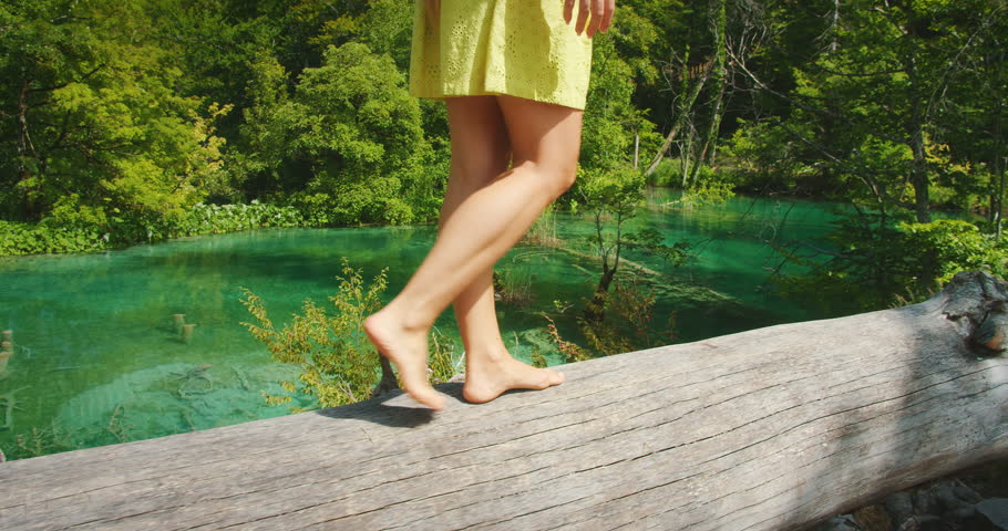 Woman walking barefoot on a log above emerald water in Plitvice Lakes National Park in Croatia