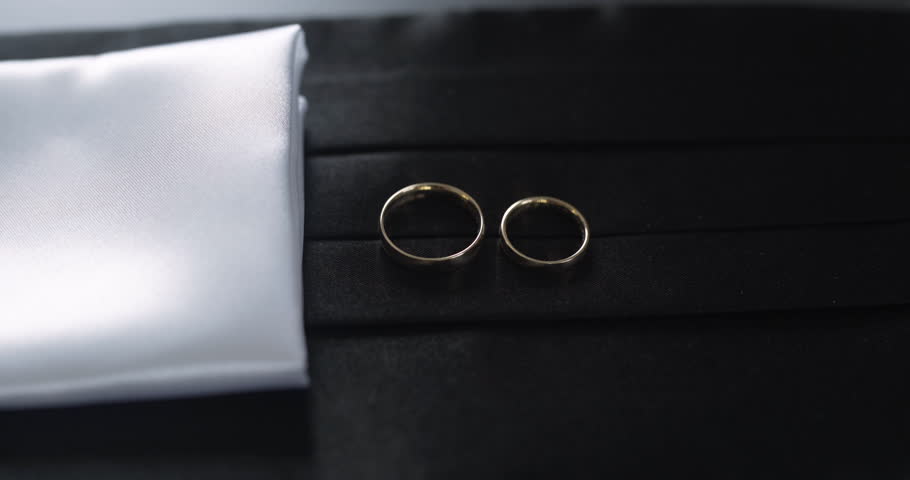Close-up of two wedding rings placed on a black strip and white pocket square, symbolizing marriage.