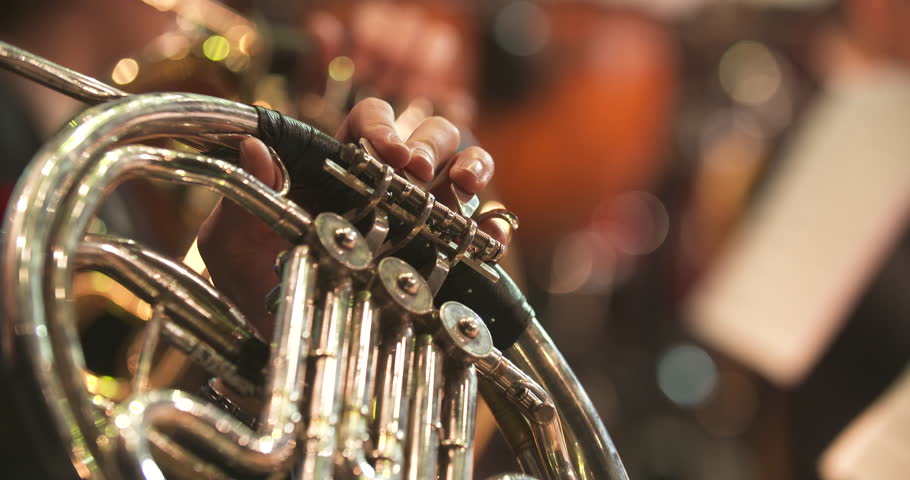 Detailed view of a man's hands skillfully playing a French horn during a classical music concert.