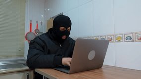 Hacker wearing balaclava is typing on a laptop in a kitchen - Powered by Shutterstock - Get 15% off with code: PIKWIZARD15