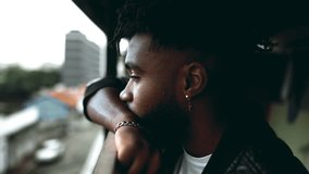One pensive young black man standing at balcony leaning on metal bar gazing at view in deep mental reflection. Contemplative close-up face of thoughtful person of African descent - Powered by Shutterstock - Get 15% off with code: PIKWIZARD15