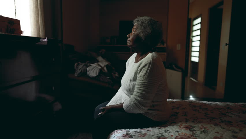 Lonely South American elderly lady sitting by bedside with peace tranquil gaze at window inside dimly lit humble bedroom contemplating life and past memories. senior 80s person