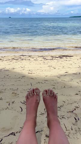 Vertical 4K b roll video of bare feet outdoor at daytime on the beach with blurry blue ocean background on the tropical Siargao island during a summer vacation in the Philippines in Asia.