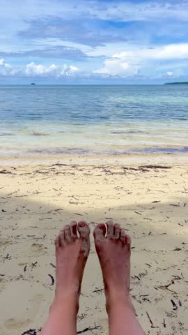 Vertical 4K b roll video of bare feet outdoor at daytime on the beach with blurry blue ocean background on the tropical Siargao island during a summer vacation in the Philippines in Asia.