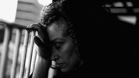 One pensive sad black woman closing eyes in sorrow struggling with depression leaning on metal bar by balcony struggles quiet despair at home in dramatic black and white, monochrome - Powered by Shutterstock - Get 15% off with code: PIKWIZARD15