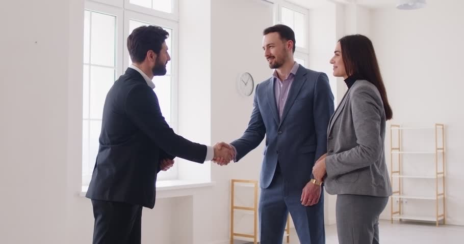 Couple customers shaking hands with realtor after successful deal or signing contract, standing in new apartment they bought, greeting new homeowners. Real estate market and mortgage concept