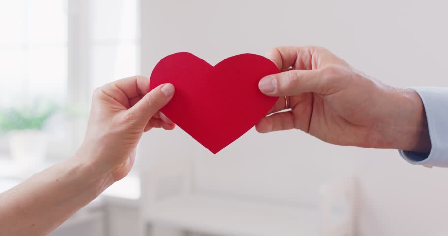 Two hands holding red paper heart, symbolizing love, care and emotional connection. Meaningful gesture expressing kindness, warmth and support, representing romance, friendship or charity concept.