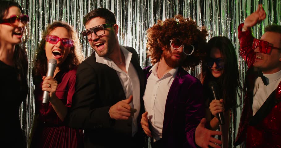 slow motion video of a group of happy smiling young people singing song into microphones having fun at disco party together at karaoke club. Funny friends dancing in modern nightclub. 4k video.