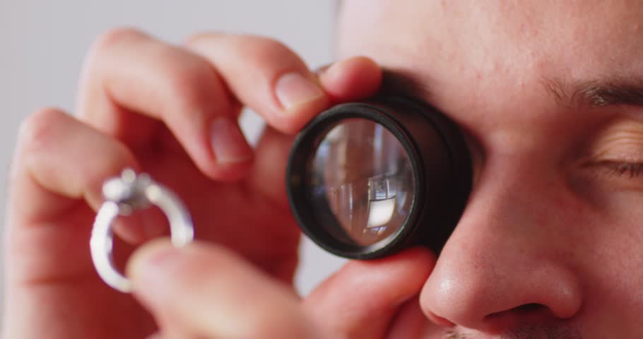 Close up of male jeweler examining expensive diamond ring through magnifying loupe. Professional appraiser checking value, clarity, quality and authenticity of precious gemstone with magnifying glass.