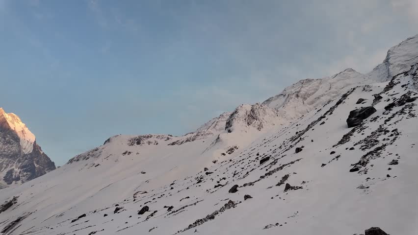 4k video footage Snow-capped Himalayan peaks visible during sunset or sunrise at Annapurna Base Camp, Nepal with blue sky and white clouds background. Rocky mountains and snowy cliffs at dusk or dawn.