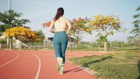 A woman is running on a track. She is wearing a white tank top and blue pants. The track is red and surrounded by trees - Powered by Shutterstock - Get 15% off with code: PIKWIZARD15