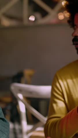 Vertical HD video of happy African American male paying with a smartwatch in a restaurant. Male seller holding a payment machine.