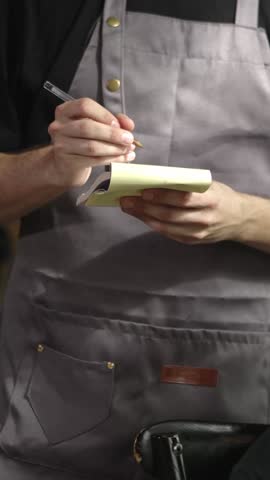 Vertical HD video. Close up of young waitress male hands taking order from group of friends at restaurant. Small business and people concept.