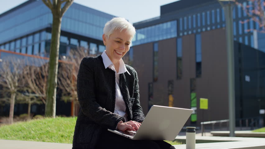 Happy senior woman working on laptop outdoors