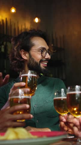Vertical HD video of young group of diverse friends enjoying weekend together cheering with beers at brewery bar - International friendship concept
