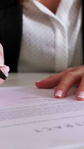 Vertical HD video of young professional woman carefully signing critical legal contract. Close-up view of a businesswoman diligently signing a legal document at her office desk