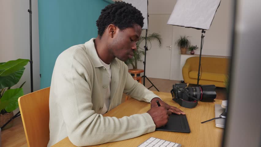 Professional young African photographer retouching photos with a graphics tablet in his modern studio. Creative occupation and business concept