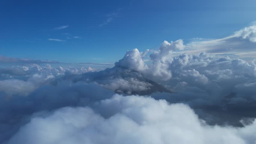 Dramatic aerial shot of Mount Inerie covered by clouds. Serene blue sky meets volcanic peaks hidden beneath a fluffy white blanket. Perfect for nature, travel, or cinematic edits.