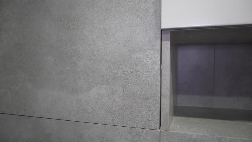 Gray concrete tiles create a modern and minimalist backdrop for a recessed shelf in a contemporary bathroom, showcasing elegant design and functionality