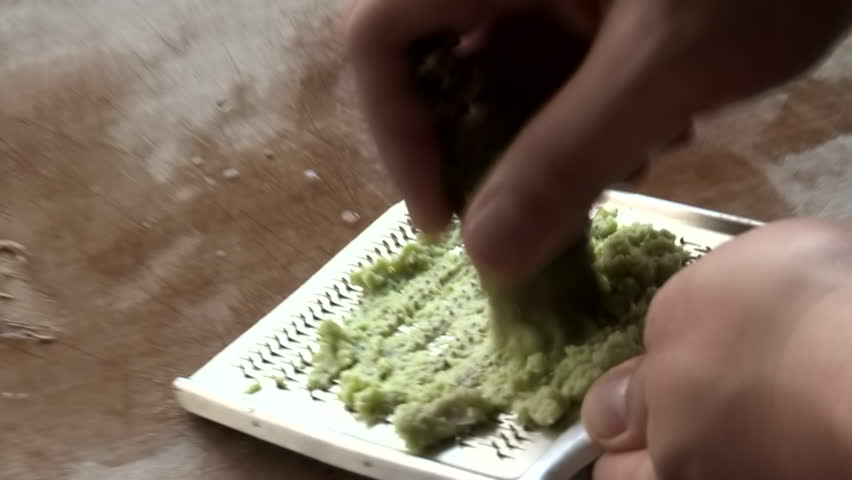 Hands grating fresh wasabi root on metal grater, green paste forming, traditional Japanese culinary preparation, spicy condiment for sushi and sashimi