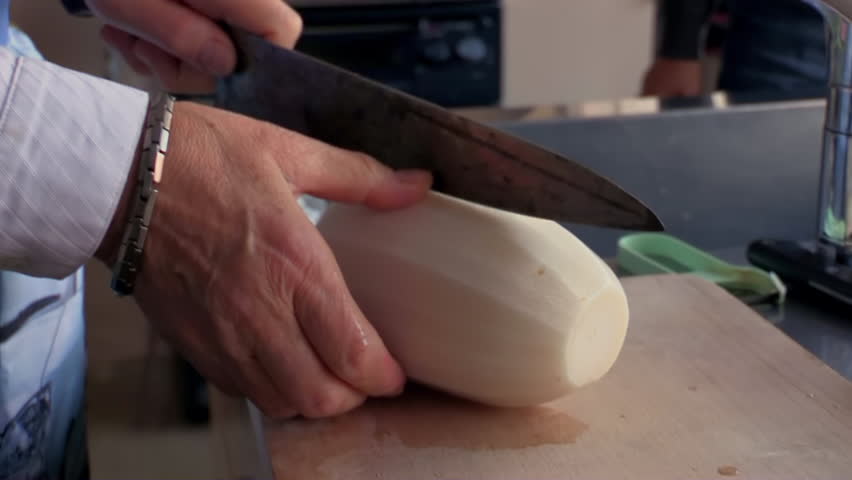 Hands slicing fresh daikon radish on wooden cutting board, home kitchen preparation, root vegetable cooking, traditional meal prep, knife cutting technique, food process