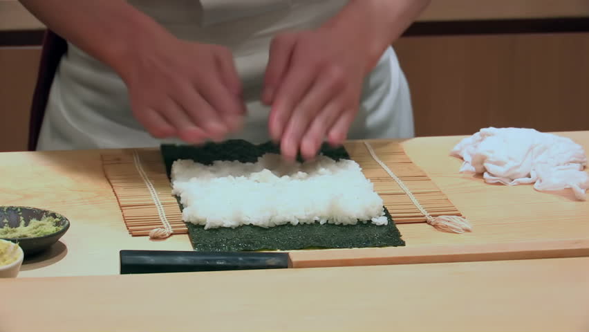 Laying sushi rice on seaweed sheet, precise hand movements, traditional sushi-making process, Japanese cuisine preparation, bamboo mat, attention to detail in culinary craft