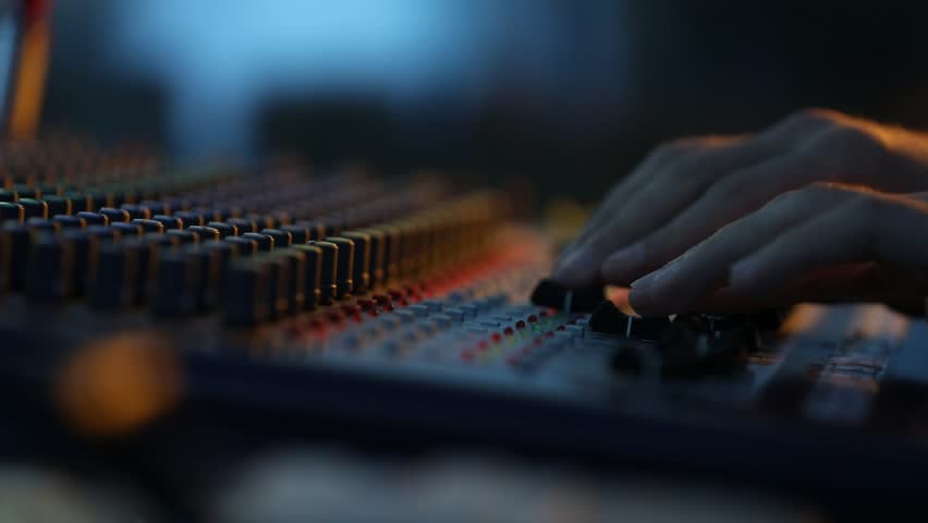 Close-up of sound technician adjusting levels on audio mixing console. Red light, sound check at the nightclub. Modern audio system.