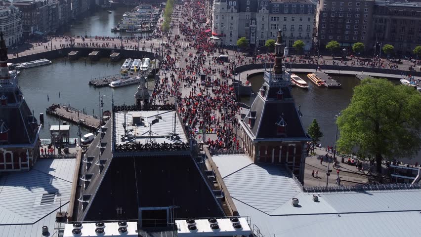 Low altitude aerial view of Amsterdam city center during King's Day the Damrak is an avenue and partially filled in canal downtown running between the Central railway station and Dam Square 4k